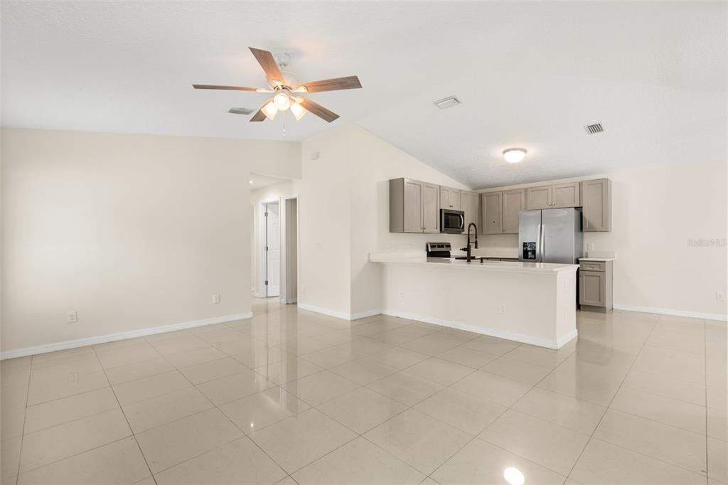An open-concept kitchen with gray cabinets and a breakfast bar overlooks a tiled living area — 339 CHINABERRY AVENUE, OVIEDO, FL