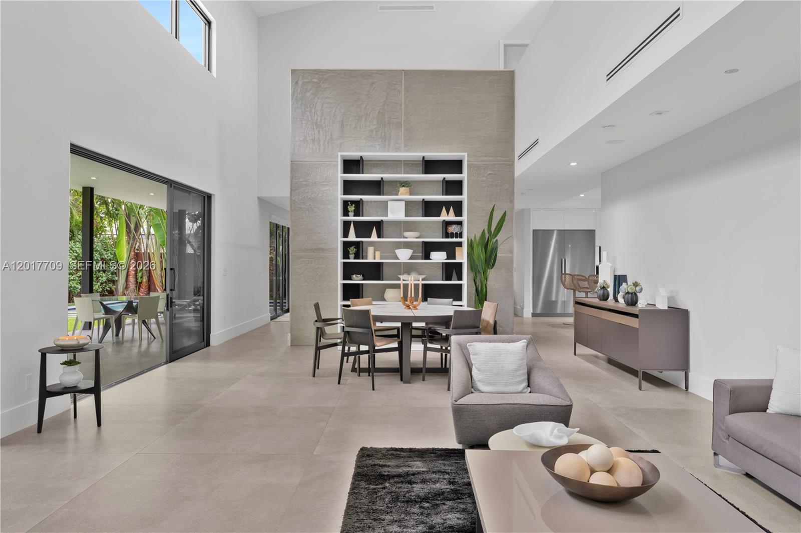 A modern, high-ceilinged living and dining area features a large concrete accent wall with shelving — 10 Samana Dr, Miami FL 33133, MIAMI, FL