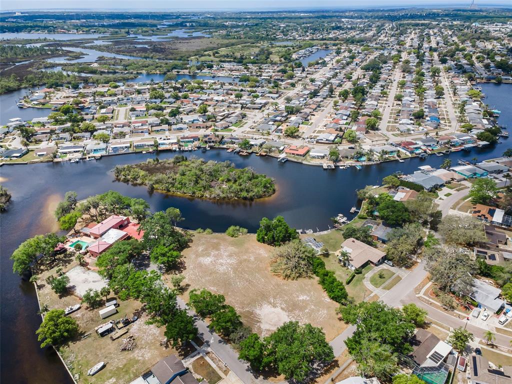 An aerial view shows a vacant waterfront lot surrounded by residential homes and canals — FLOTILLA, HOLIDAY, FL
