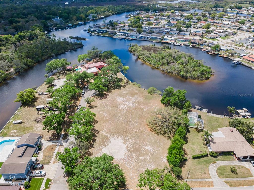 An aerial view shows a large, cleared vacant lot situated between two waterfront residential properties — FLOTILLA, HOLIDAY, FL