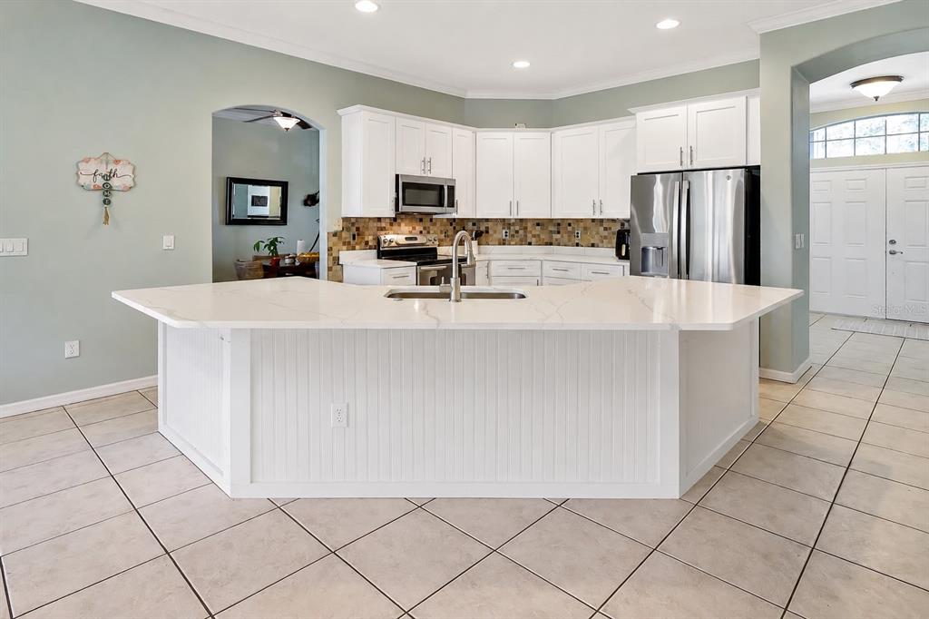A kitchen features white cabinets, a large island with a quartz countertop, and tiled flooring — 115 EMPIRE TERRACE, SEBASTIAN, FL