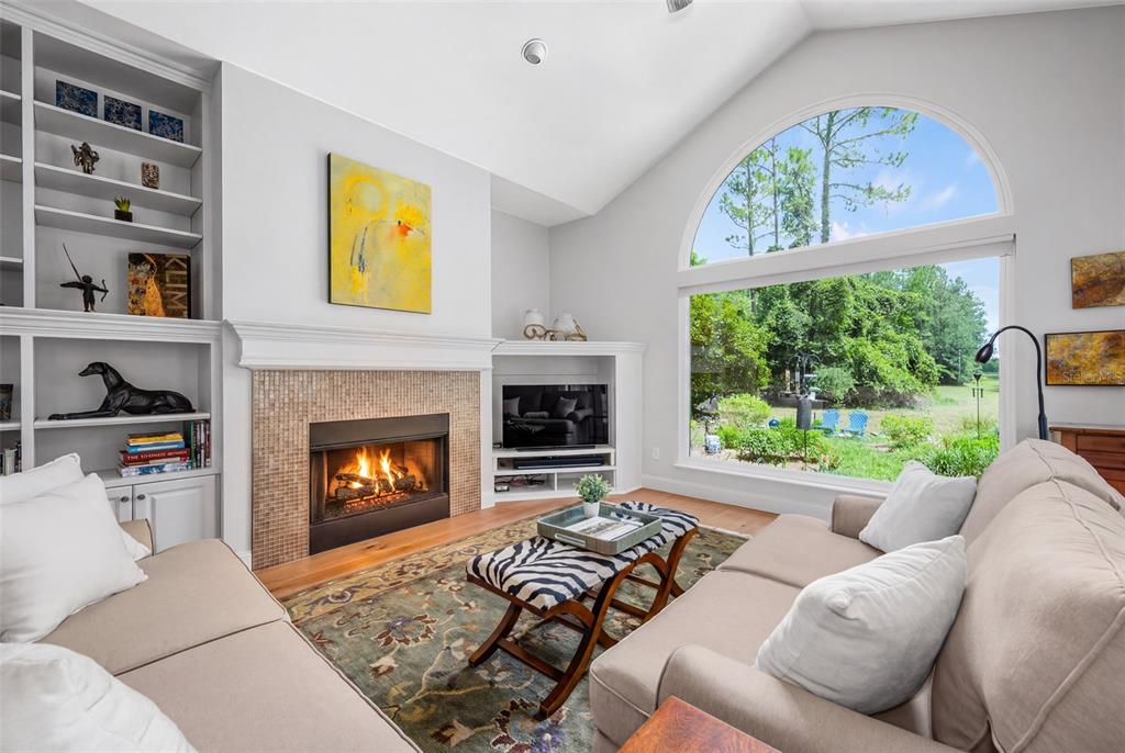 A living room features a fireplace, built-in shelving, a zebra-print ottoman, and a large arched window — 9340 SW 32ND PLACE, GAINESVILLE, FL