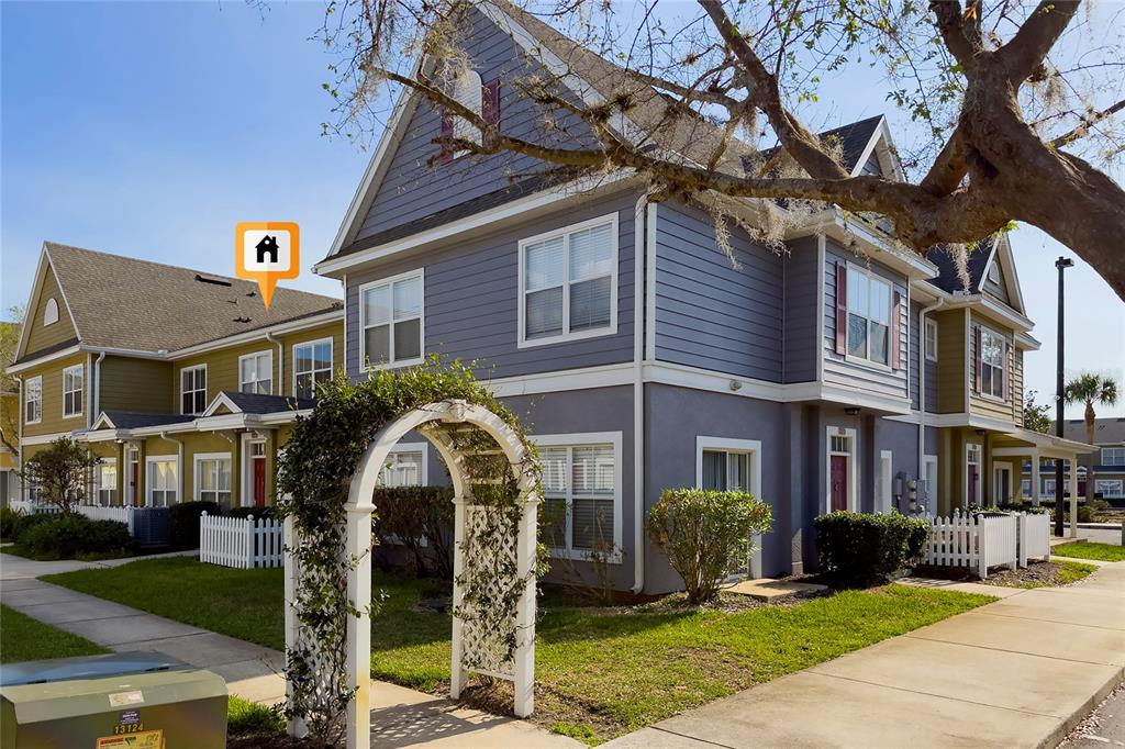 A multi-story townhouse complex with gray and green siding, white trim, and a garden arch — 2611 GALA ROAD N UNIT 106, KISSIMMEE, FL