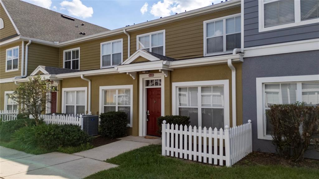 A two-story townhouse exterior features olive-colored siding, a red front door, and white picket fences — 2611 GALA ROAD N UNIT 106, KISSIMMEE, FL