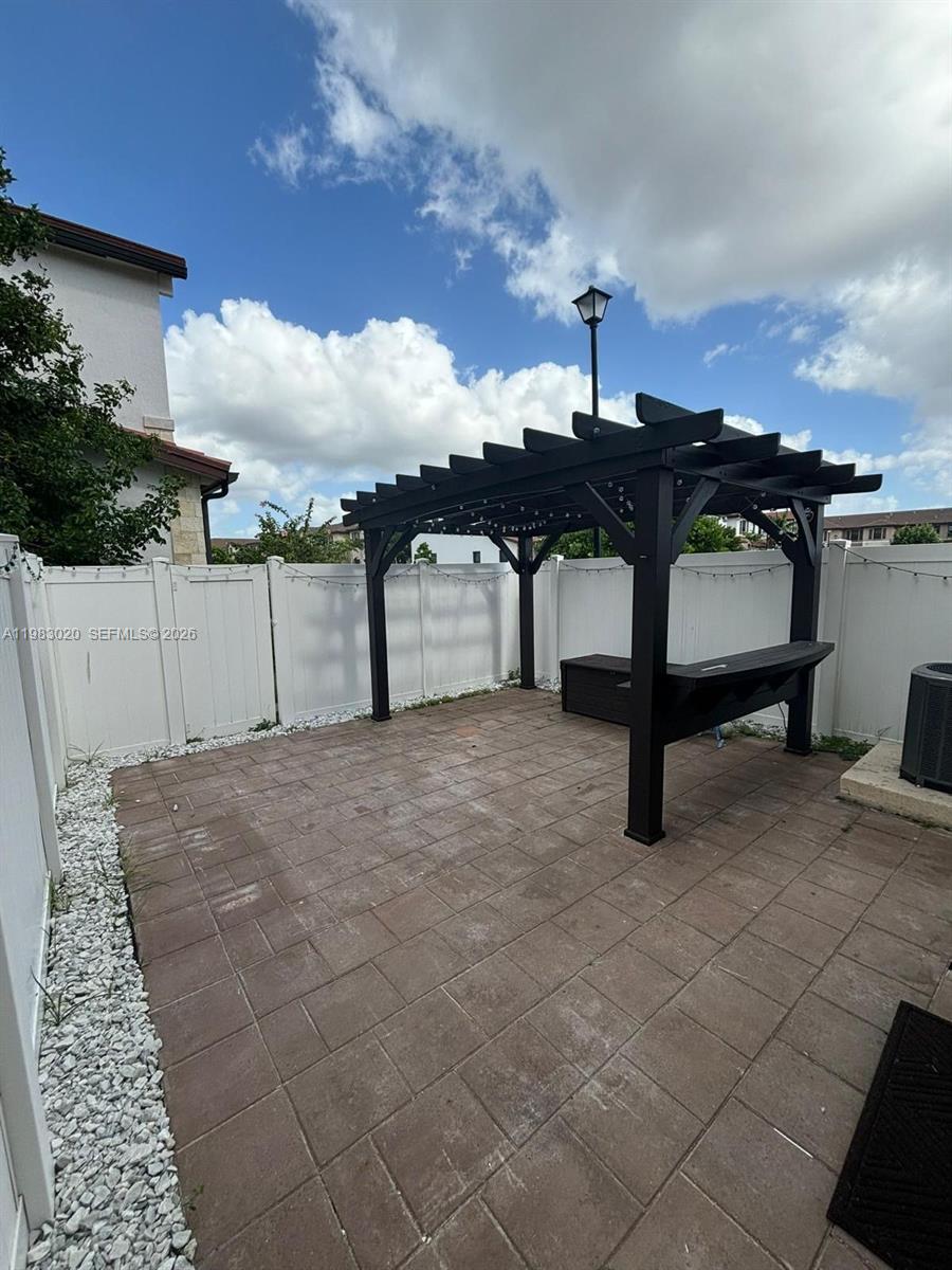 A black wooden pergola stands on a paved patio enclosed by a white vinyl fence — 3337 W 105th Ter, Hialeah FL 33018, HIALEAH, FL