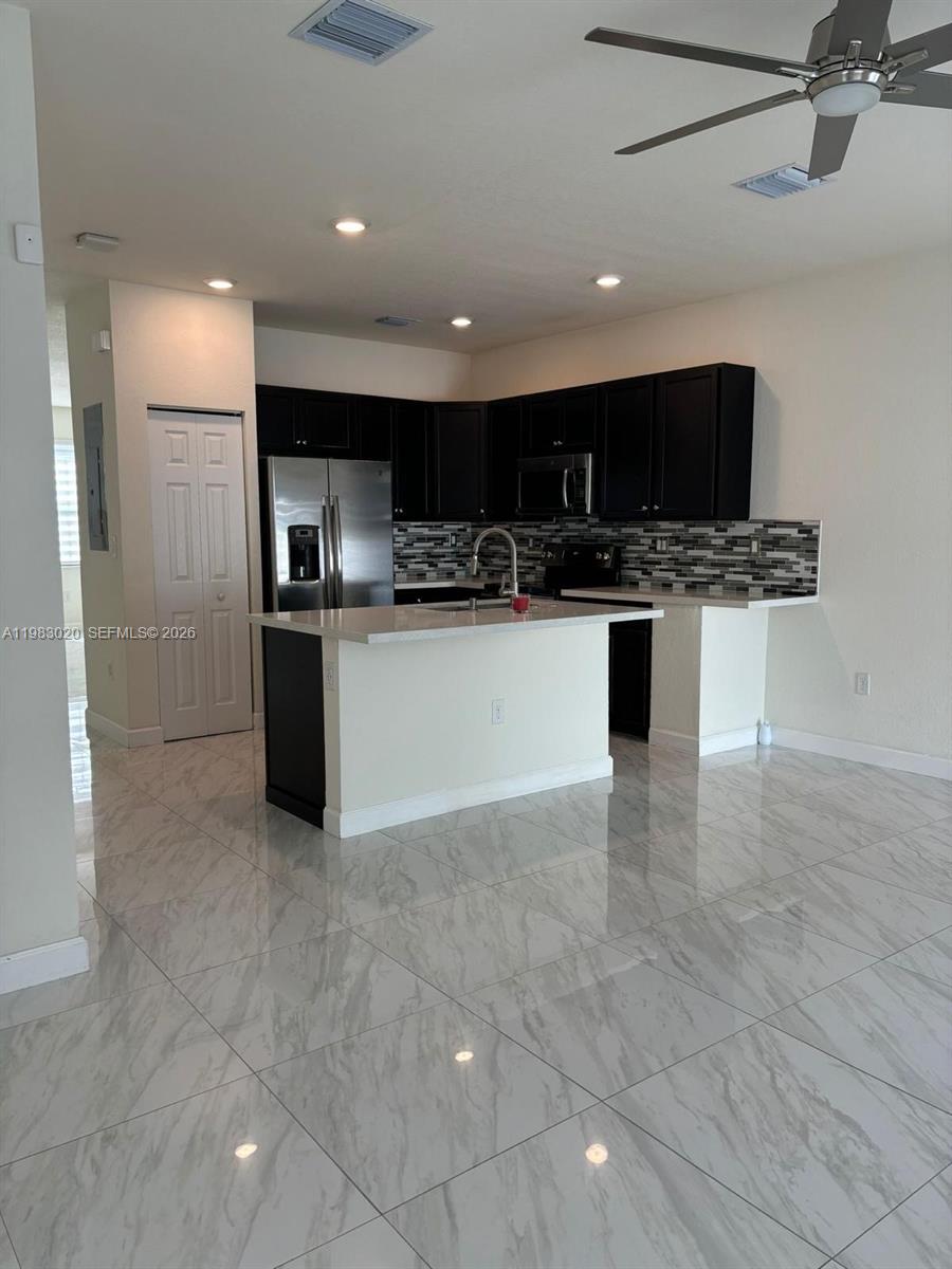 A kitchen features dark cabinets, stainless steel appliances, a white island, and light-colored tile flooring — 3337 W 105th Ter, Hialeah FL 33018, HIALEAH, FL