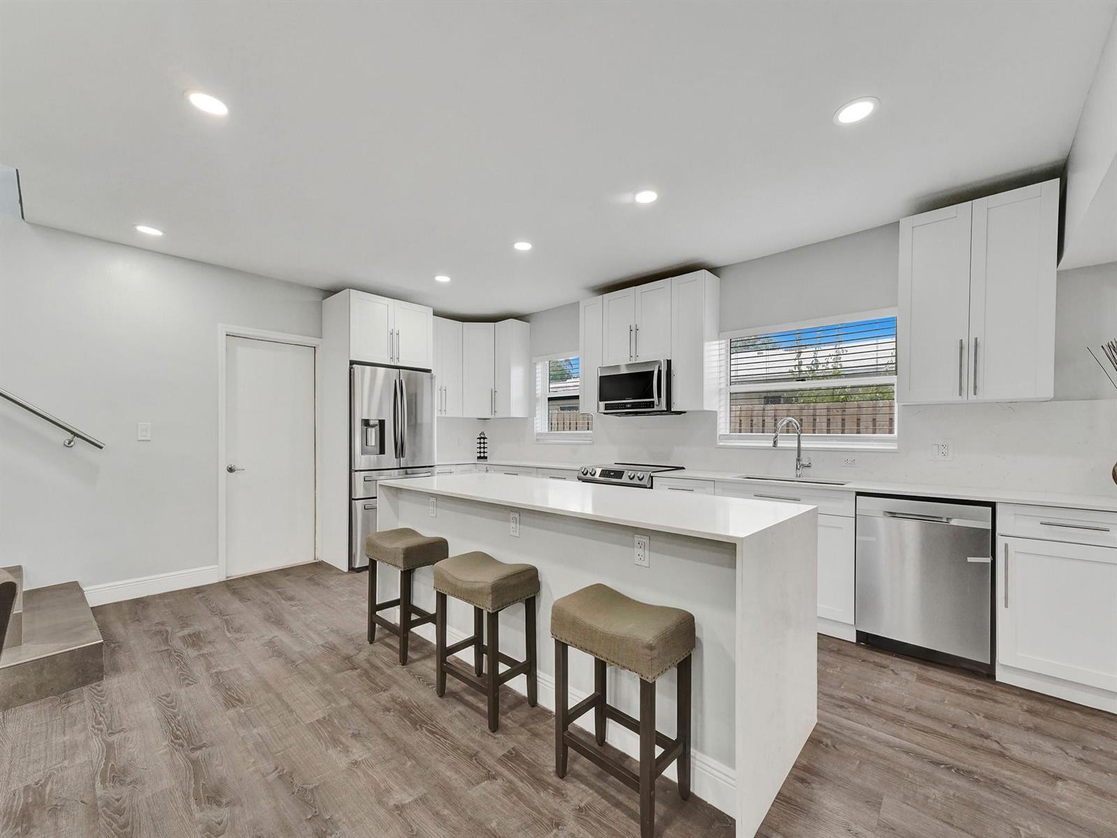 A modern kitchen features white cabinets, stainless steel appliances, a quartz island, and wood flooring — 3261 Aqua Vista Drive, Pompano Beach FL 33062, POMPANO BEACH, FL
