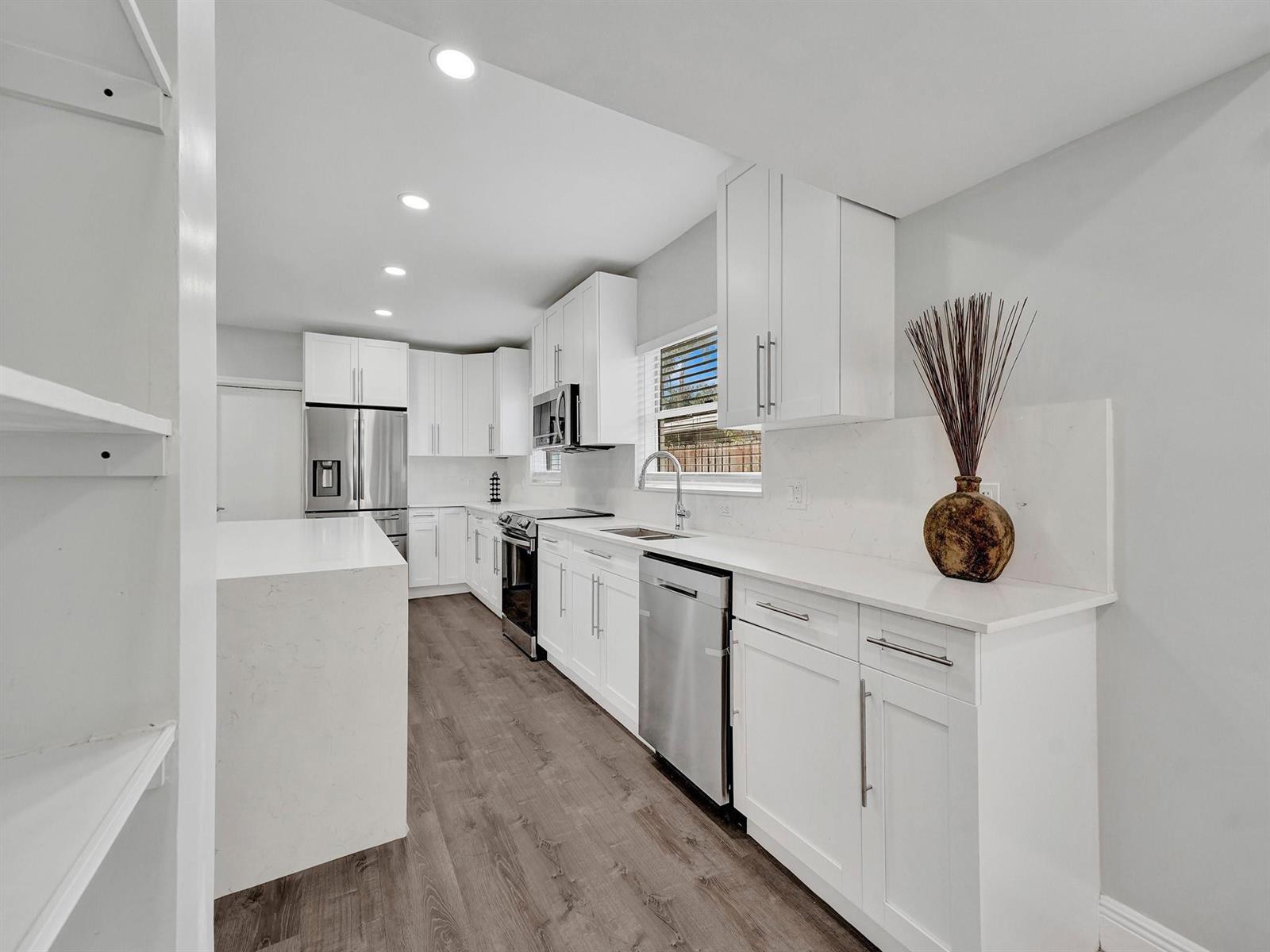 A modern kitchen features white cabinets, quartz countertops, stainless steel appliances, and wood-look flooring — 3261 Aqua Vista Drive, Pompano Beach FL 33062, POMPANO BEACH, FL