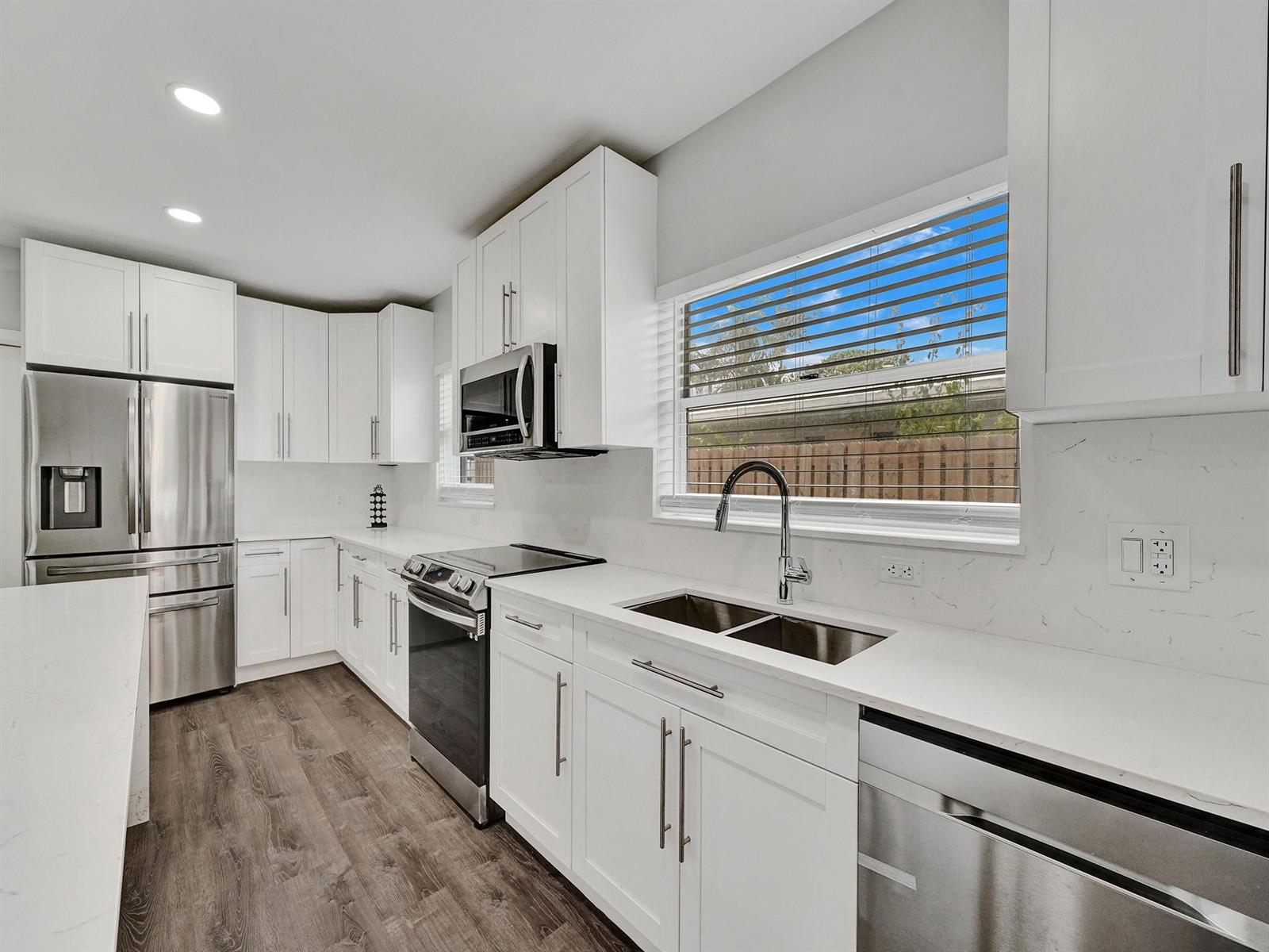 A modern kitchen features white cabinets, stainless steel appliances, quartz countertops, and wood-look flooring — 3261 Aqua Vista Drive, Pompano Beach FL 33062, POMPANO BEACH, FL