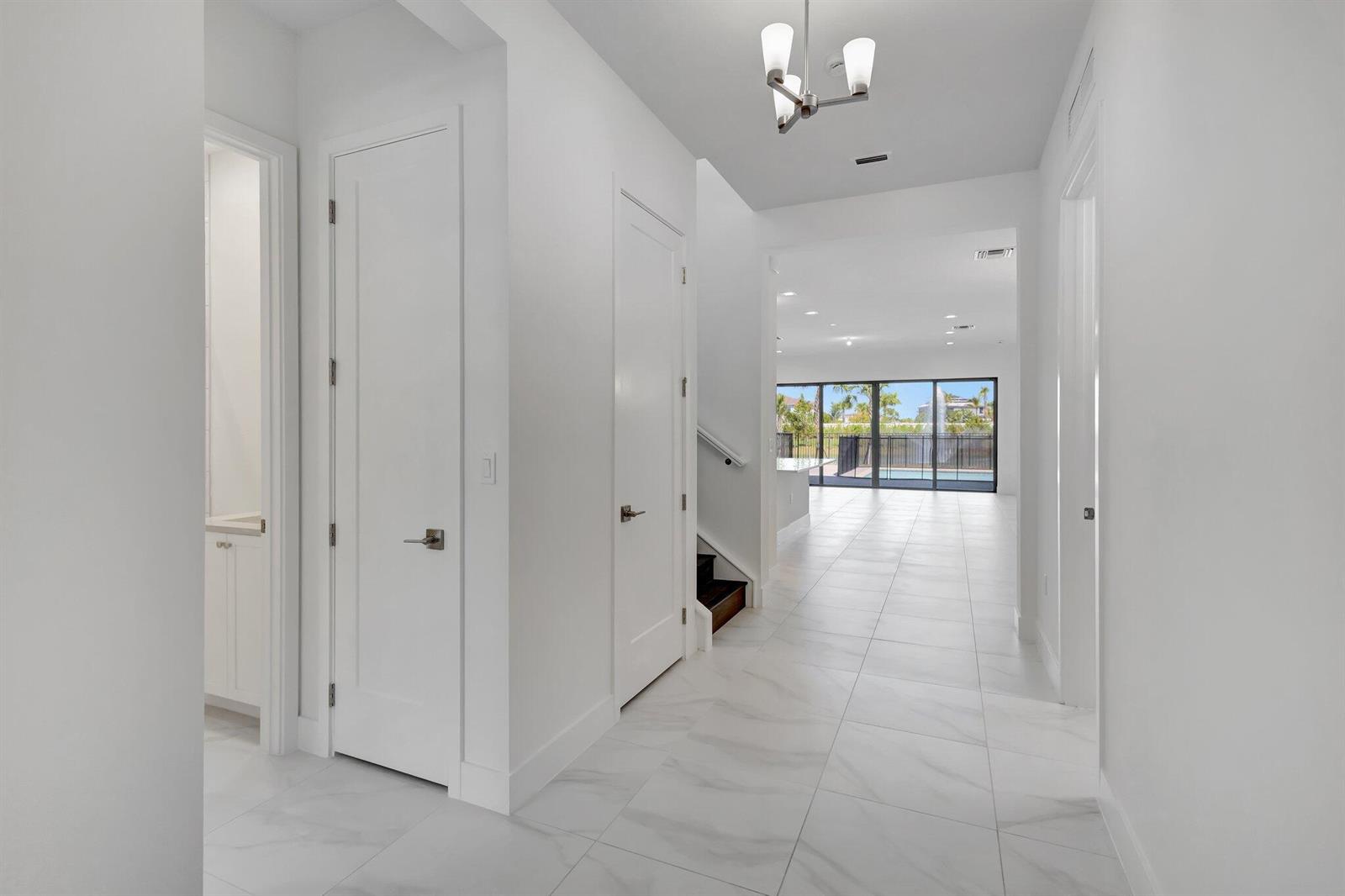 A bright hallway with white tile floors leads toward a living area with glass doors — 13079 Feathering Way, Palm Beach Gardens FL 33412, PALM BEACH GARDENS, FL