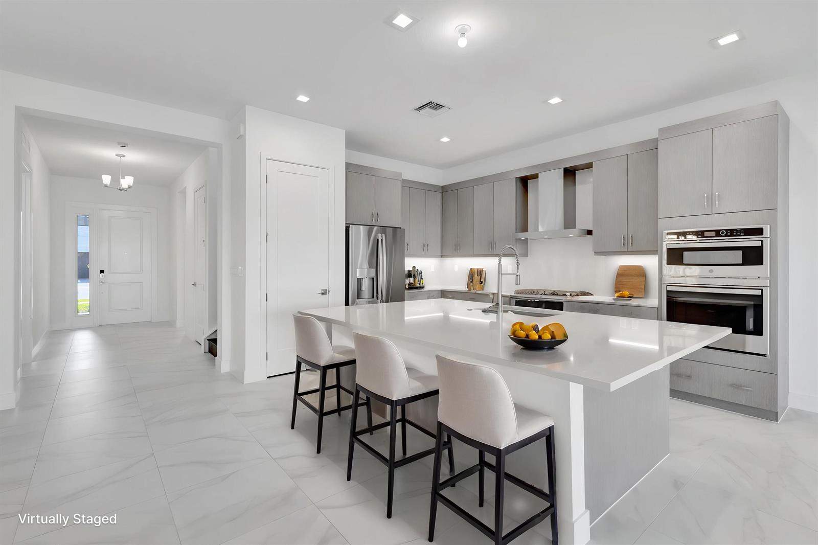 A modern kitchen features gray cabinetry, a large white island with seating, and tile flooring — 13079 Feathering Way, Palm Beach Gardens FL 33412, PALM BEACH GARDENS, FL