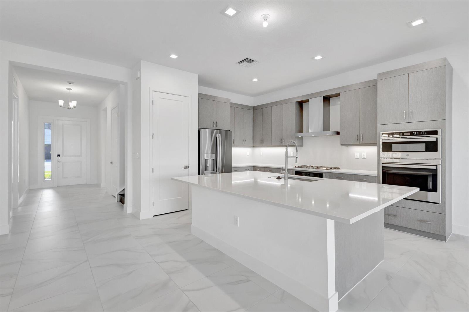 A modern kitchen features light gray cabinets, a white quartz island, and white tile flooring — 13079 Feathering Way, Palm Beach Gardens FL 33412, PALM BEACH GARDENS, FL