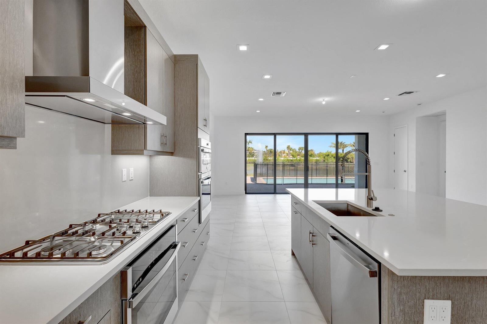 A modern kitchen features light wood cabinetry, white countertops, stainless steel appliances, and a pool view — 13079 Feathering Way, Palm Beach Gardens FL 33412, PALM BEACH GARDENS, FL