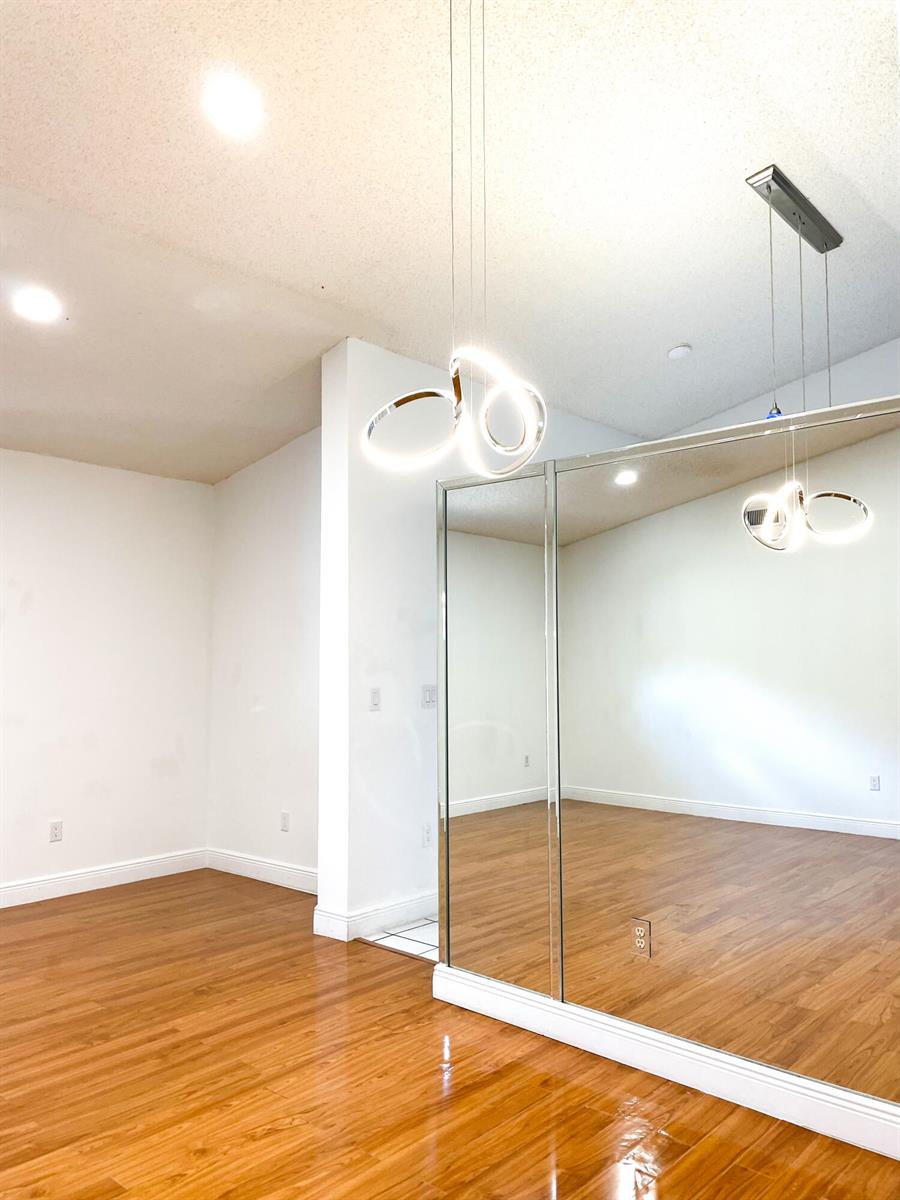 A room with wood flooring, white walls, a modern pendant light, and mirrored closet doors — 5851 Bristol Lane, Davie FL 33331, DAVIE, FL