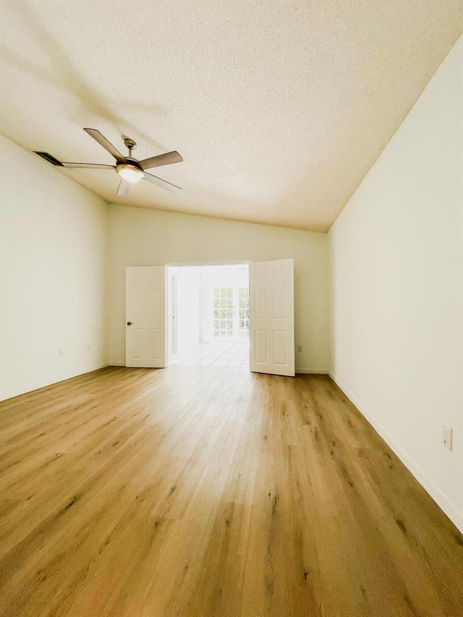 An empty room with light wood-look flooring, a ceiling fan, and double doors leading outside — 5851 Bristol Lane, Davie FL 33331, DAVIE, FL