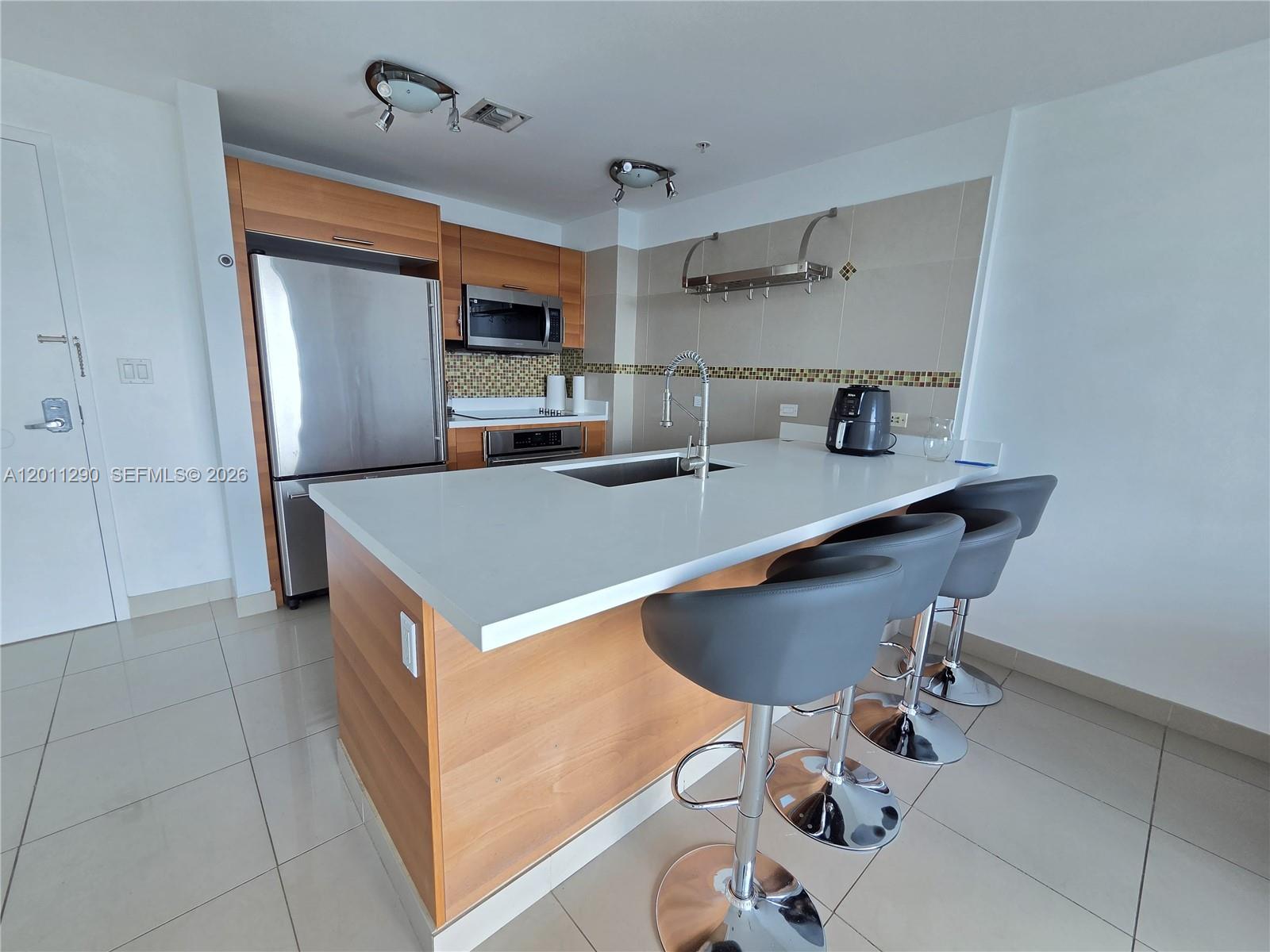 A modern kitchen features wood cabinets, stainless steel appliances, and a white island with stools — 3301 NE 1st Ave # H3005, Miami FL 33137, MIAMI, FL