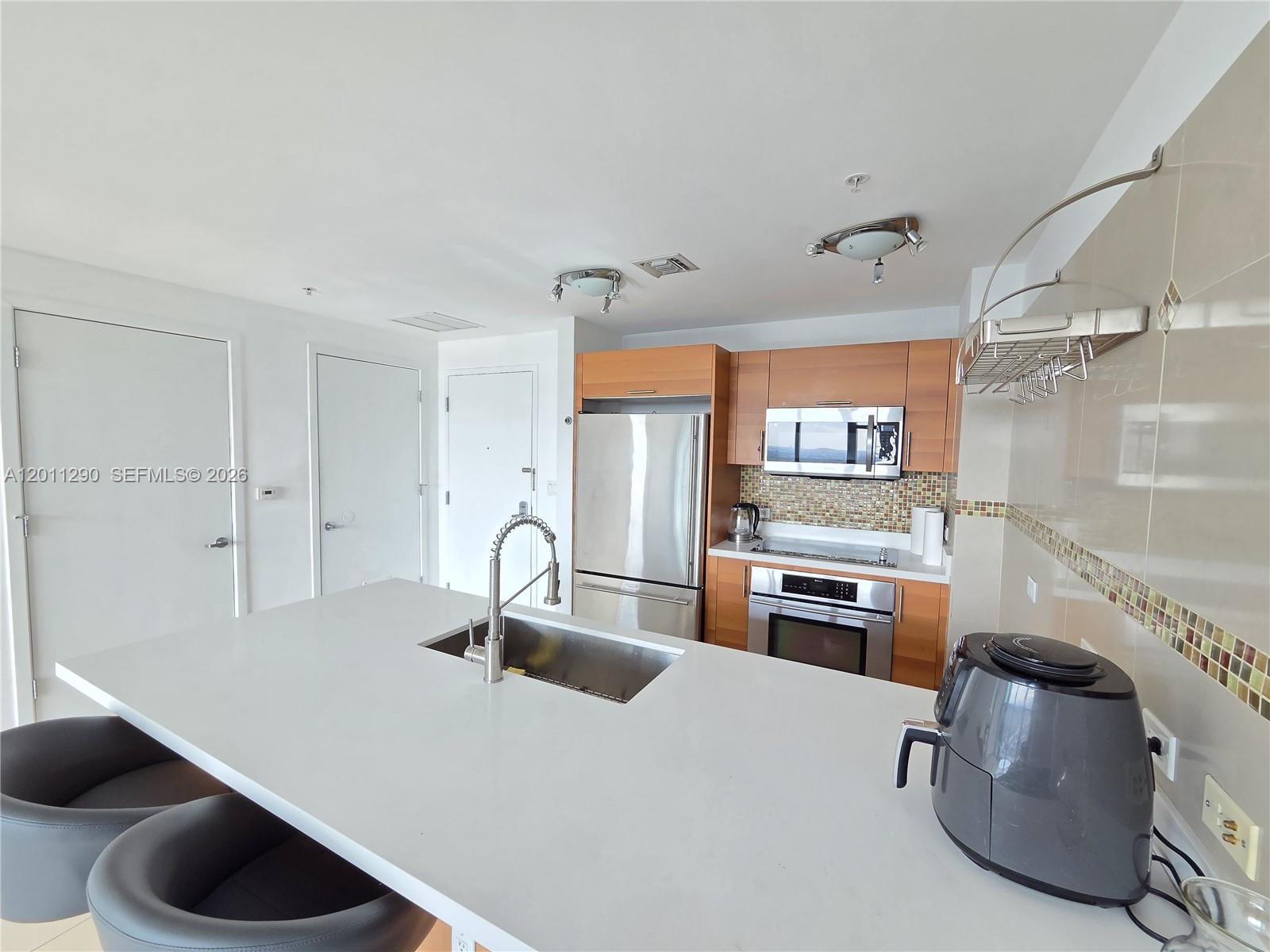 A modern kitchen features a white island, stainless steel appliances, and light wood cabinetry — 3301 NE 1st Ave # H3005, Miami FL 33137, MIAMI, FL