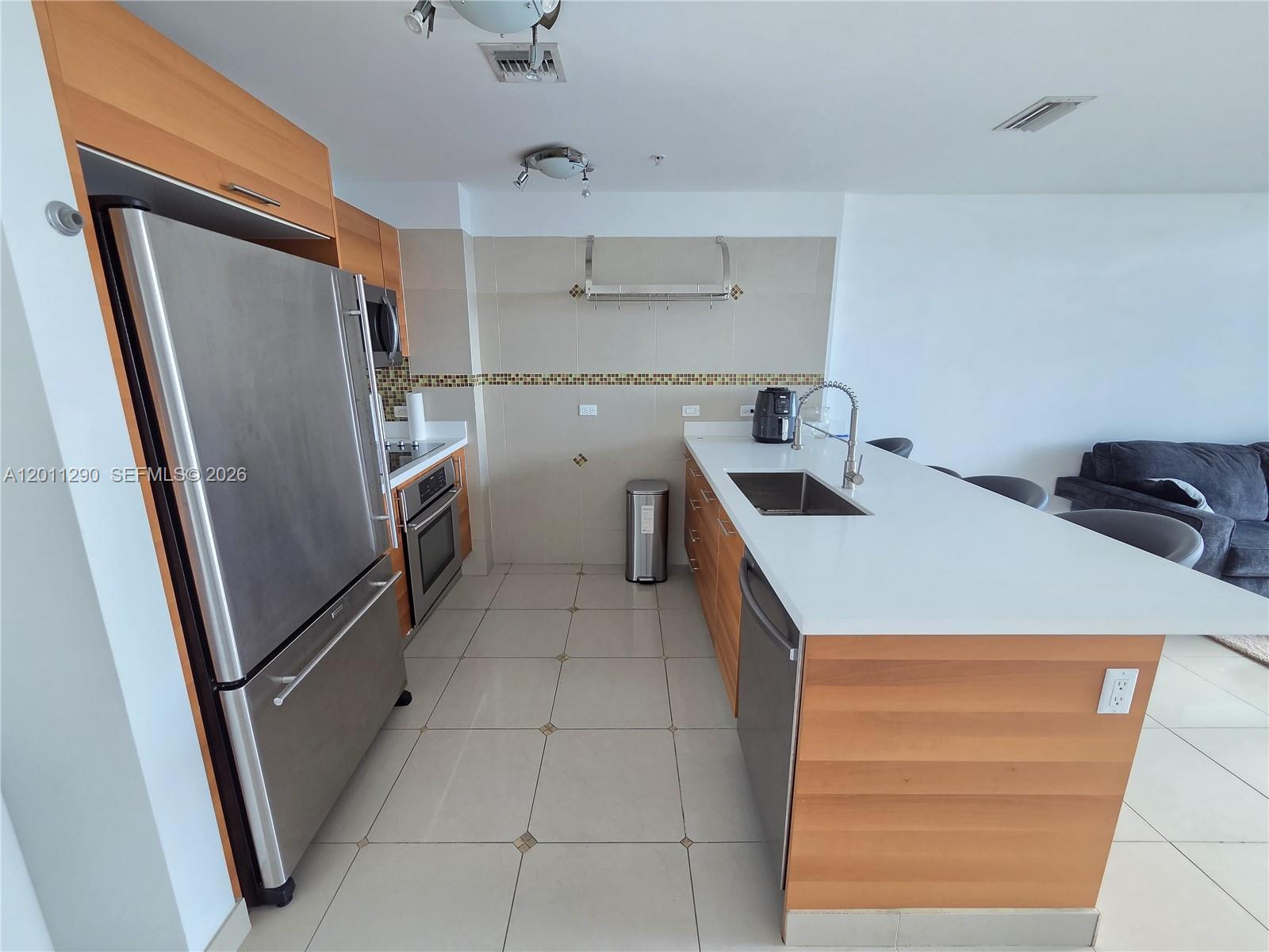 A modern kitchen features stainless steel appliances, wood cabinetry, and a white countertop island — 3301 NE 1st Ave # H3005, Miami FL 33137, MIAMI, FL