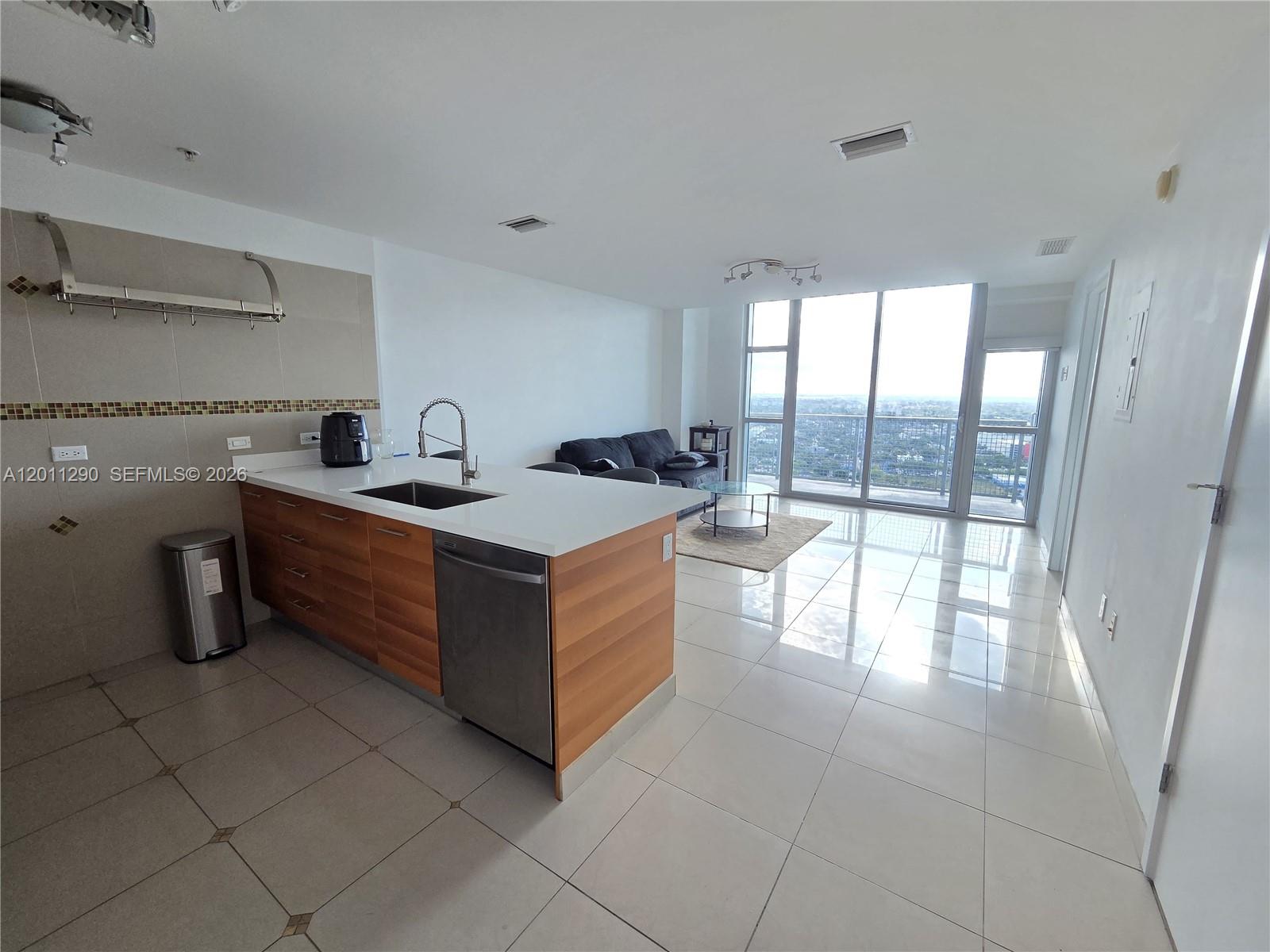A modern kitchen with wood cabinets and a white island opens into a living area — 3301 NE 1st Ave # H3005, Miami FL 33137, MIAMI, FL