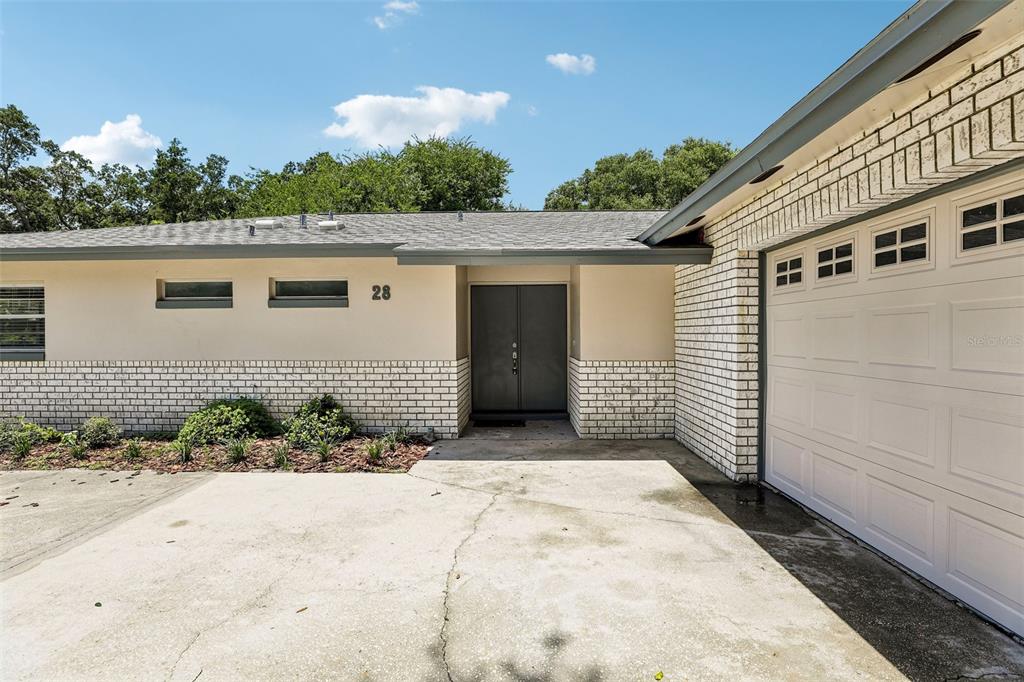 A single-story house exterior features a white brick facade, a concrete driveway, and double doors — 28 LINDA LANE, KISSIMMEE, FL