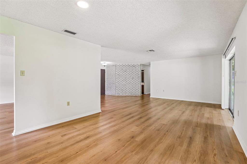 An empty living area features light wood-look flooring, white walls, and a white brick accent wall — 28 LINDA LANE, KISSIMMEE, FL