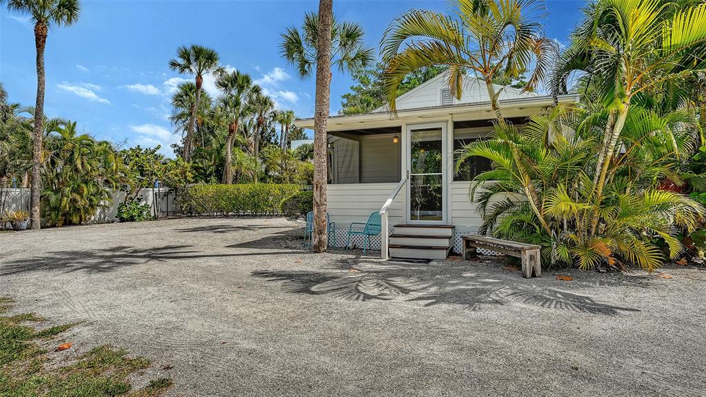 A small, light-colored cottage with a screened porch sits on a gravel lot with palm trees — 3708 SANDSPUR LANE, NOKOMIS, FL