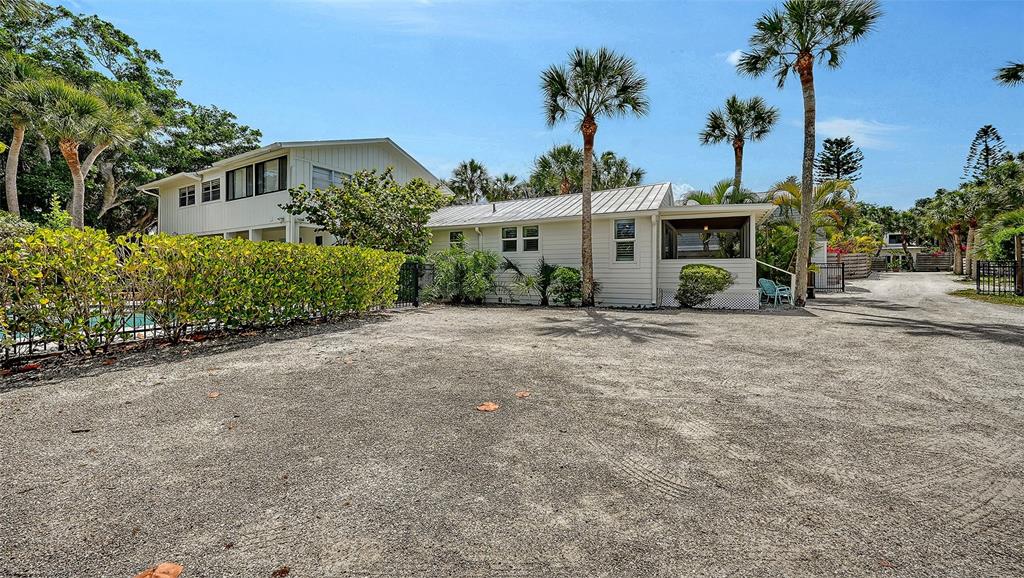 A white house with a metal roof sits behind a gravel driveway and palm trees — 3708 SANDSPUR LANE, NOKOMIS, FL
