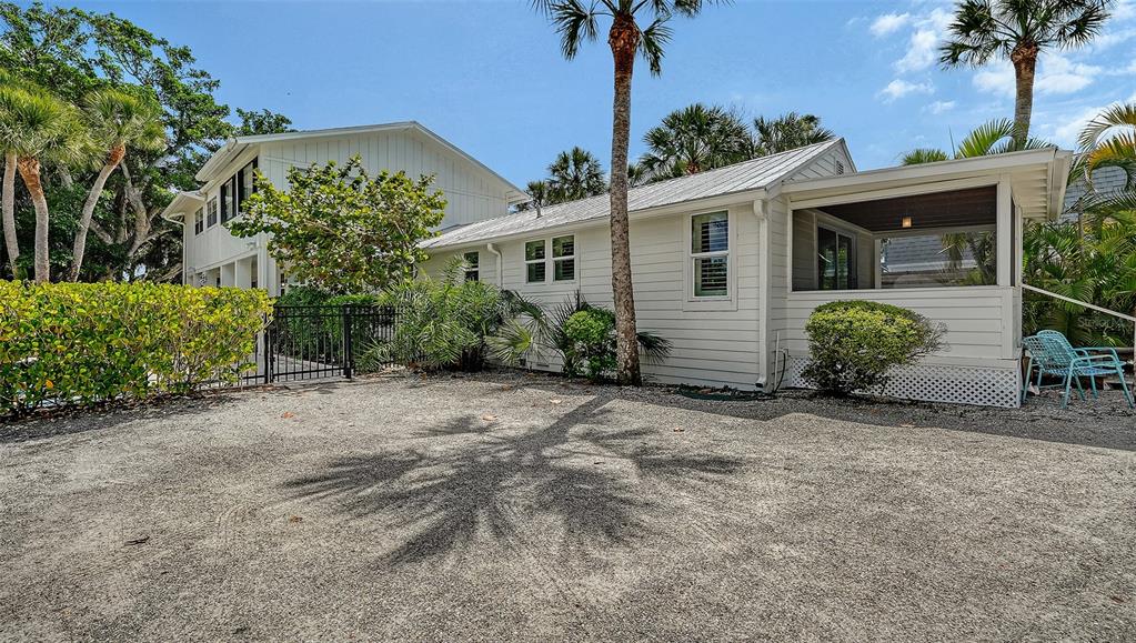 A white house with a screened-in porch sits beside a gravel driveway and palm trees — 3708 SANDSPUR LANE, NOKOMIS, FL
