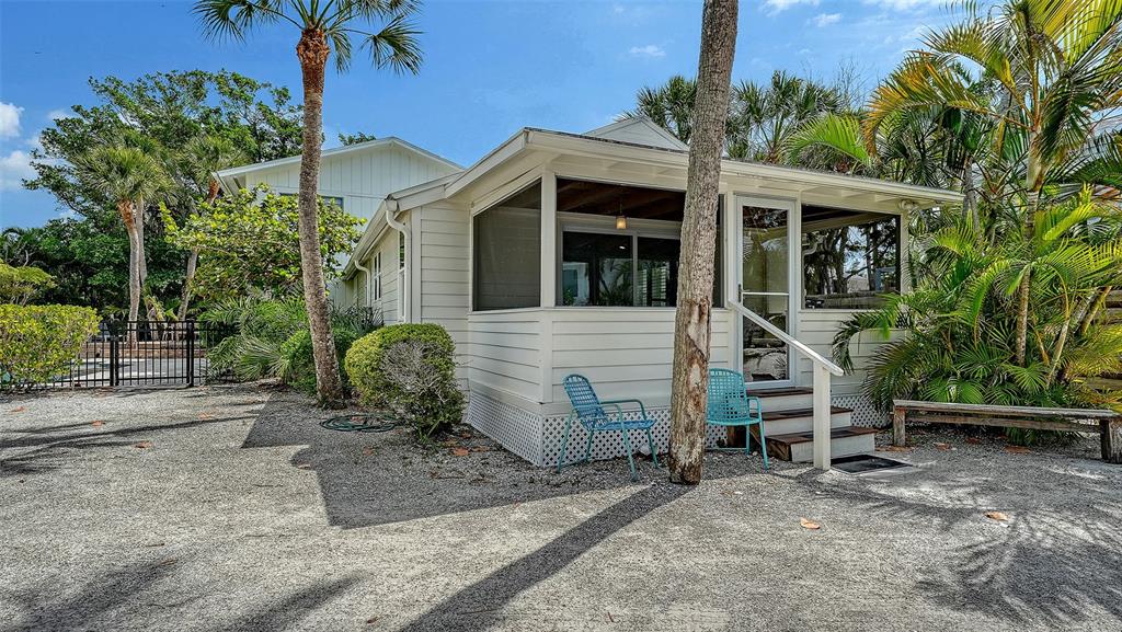 A light-colored cottage with a screened-in porch sits on a gravel lot with palm trees — 3708 SANDSPUR LANE, NOKOMIS, FL