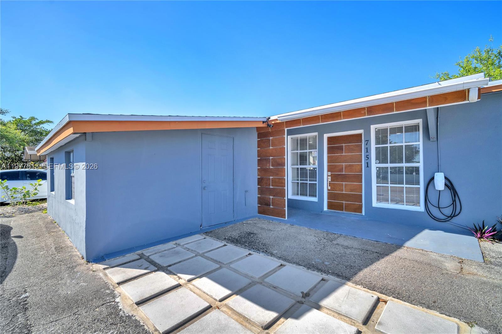 A blue exterior house features a wood-paneled front door and a paved patio area — 7151 Taft St, Hollywood FL 33024, HOLLYWOOD, FL