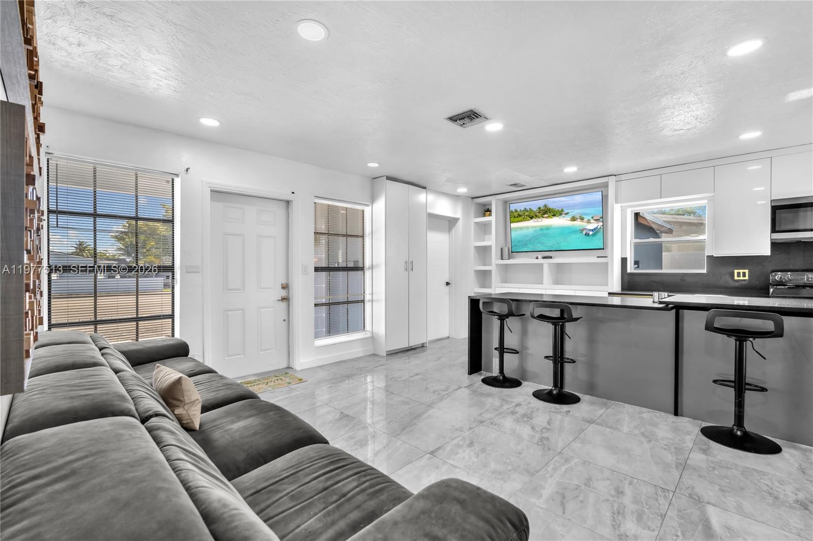A modern living room features a grey sofa, tile flooring, and an open kitchen island — 7151 Taft St, Hollywood FL 33024, HOLLYWOOD, FL