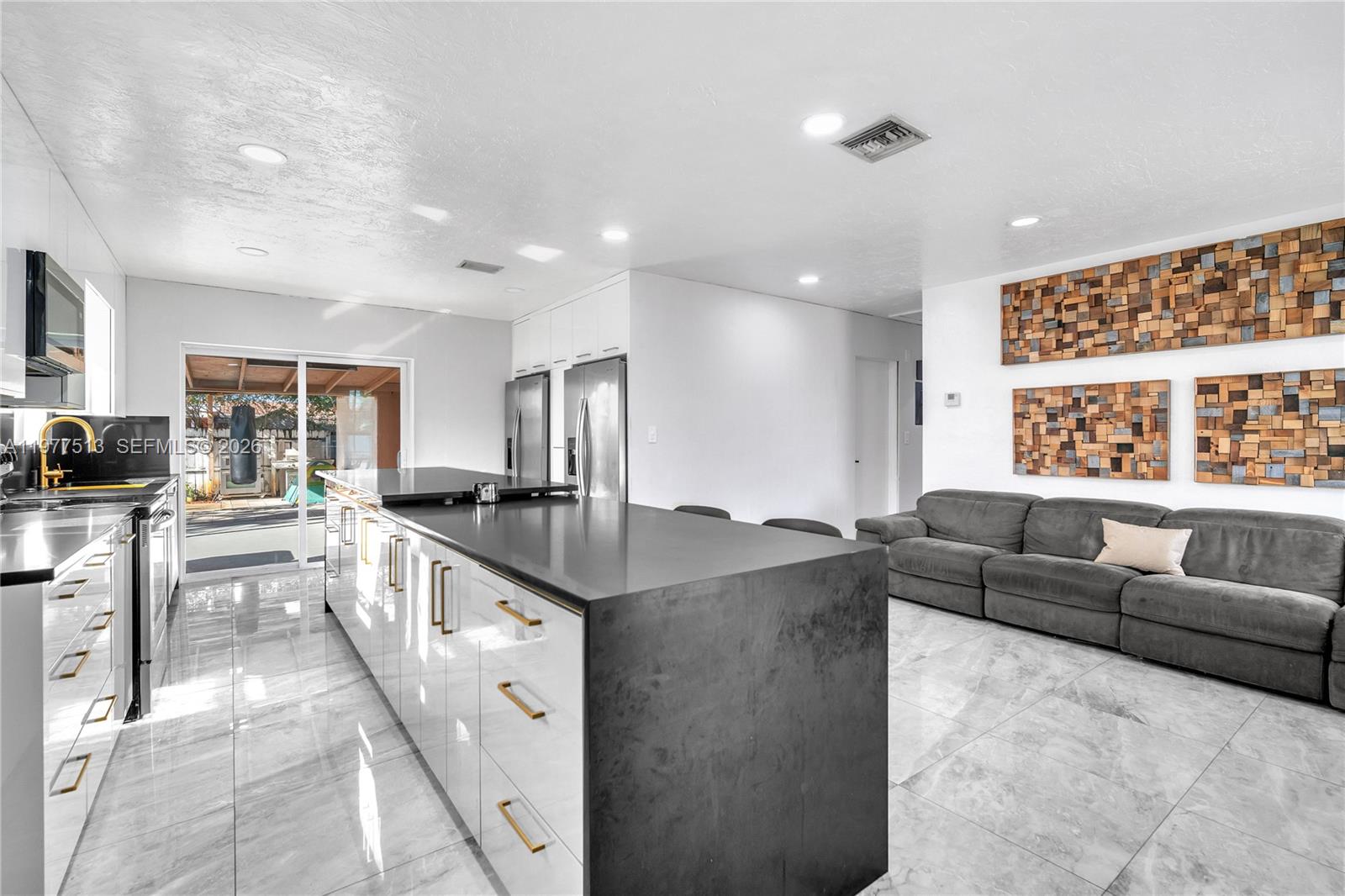 A modern kitchen with a large dark island and white cabinets opens to a living area — 7151 Taft St, Hollywood FL 33024, HOLLYWOOD, FL