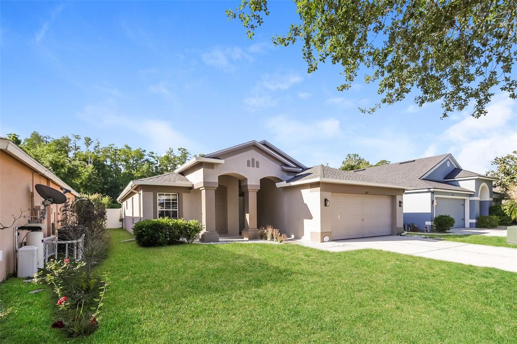 A single-story beige house with a two-car garage and a front porch under a gable — 5921 WAR ADMIRAL DRIVE, WESLEY CHAPEL, FL
