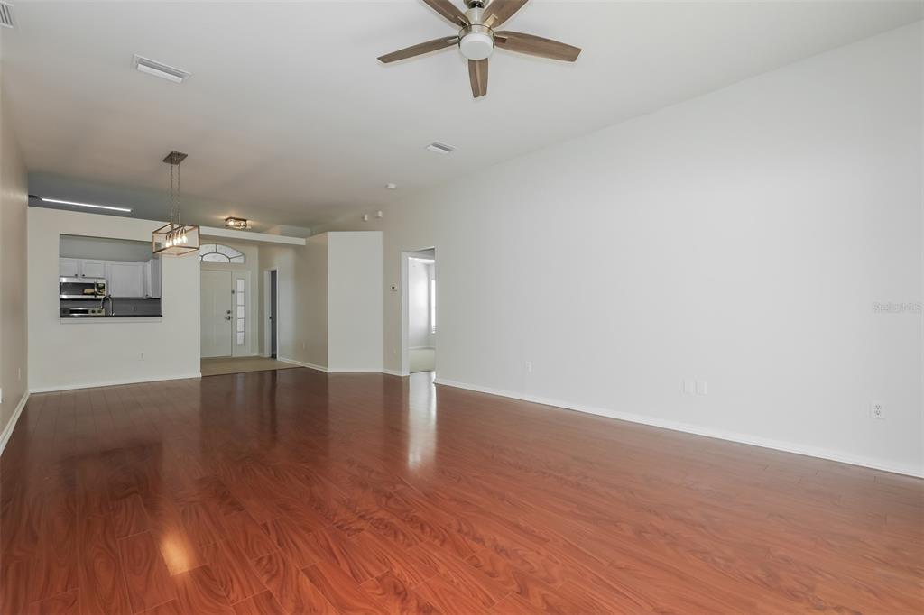 An empty living room with wood-look flooring, a ceiling fan, and an adjacent kitchen area — 5921 WAR ADMIRAL DRIVE, WESLEY CHAPEL, FL