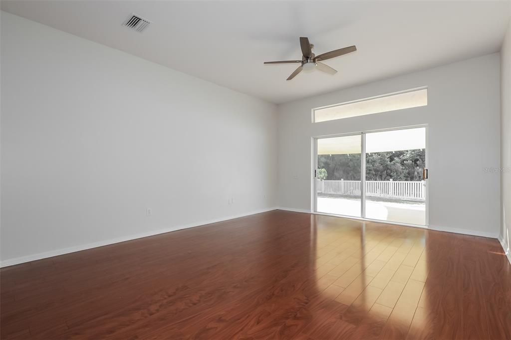 An empty room with wood-look flooring, a ceiling fan, and sliding glass doors to a patio — 5921 WAR ADMIRAL DRIVE, WESLEY CHAPEL, FL