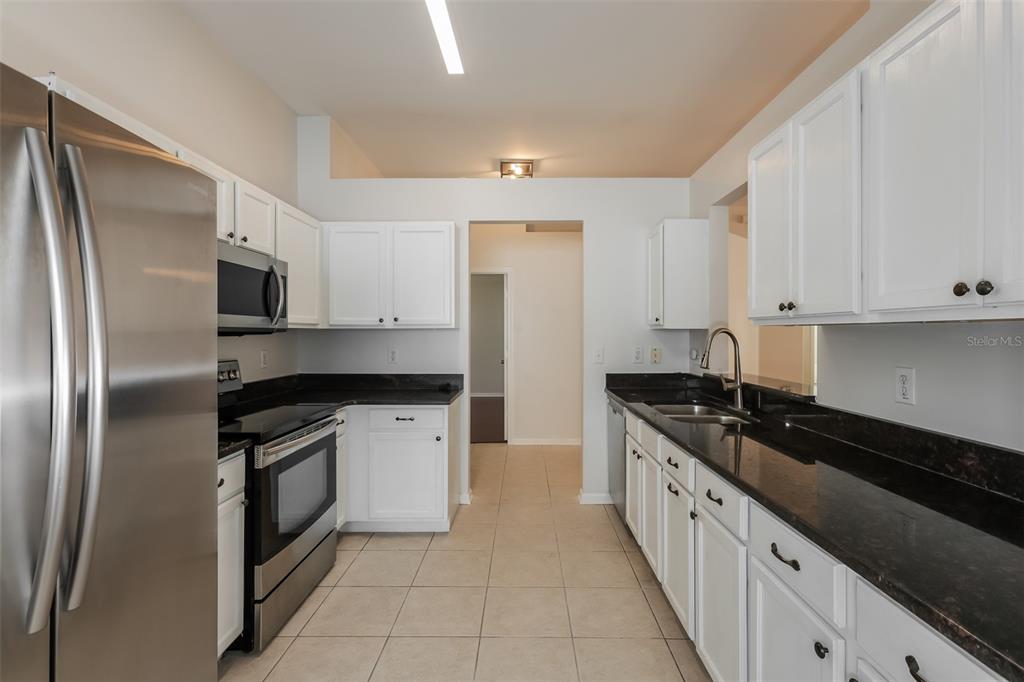 A kitchen features white cabinets, black countertops, stainless steel appliances, and light-colored tile flooring — 5921 WAR ADMIRAL DRIVE, WESLEY CHAPEL, FL