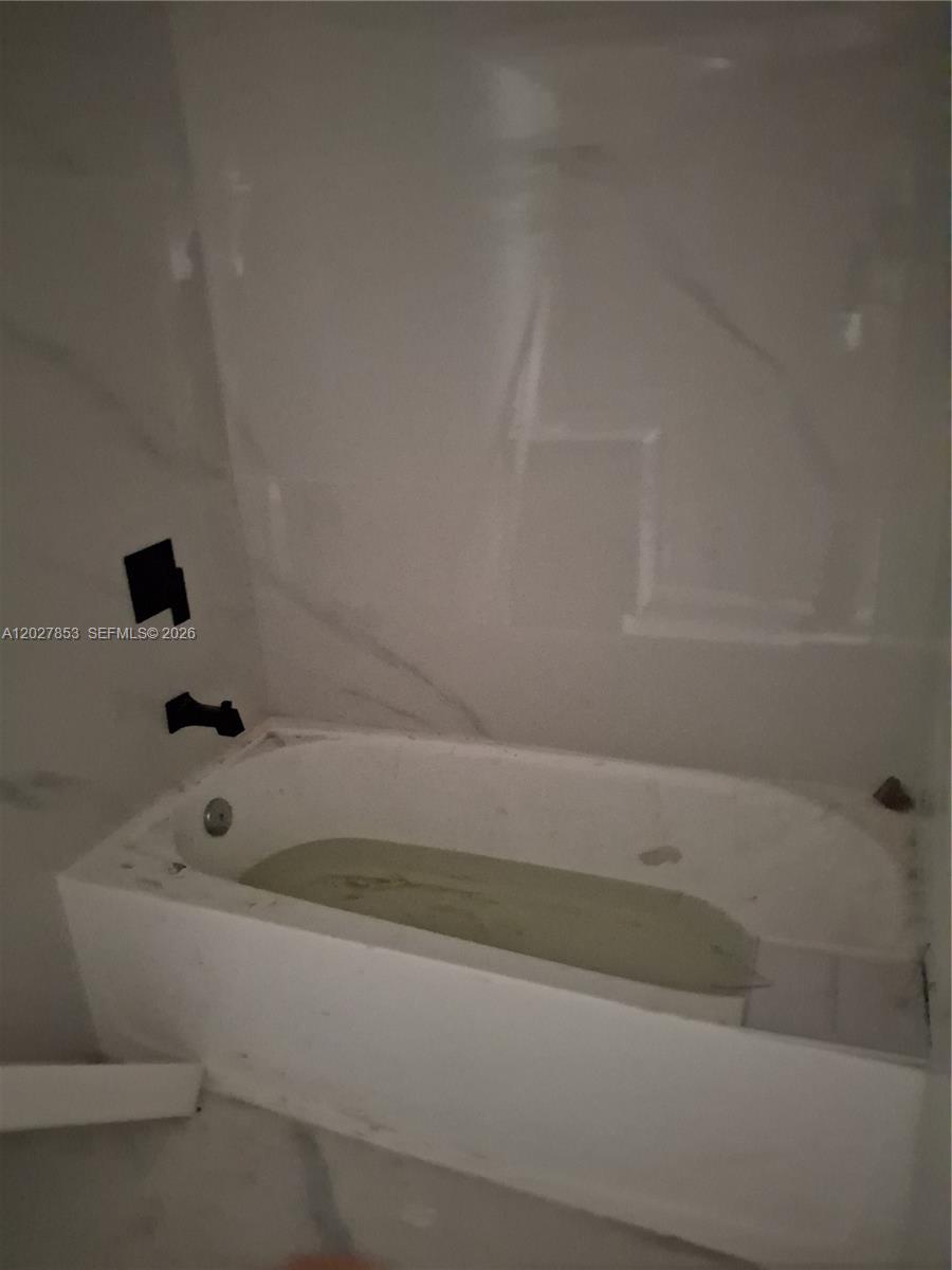 A white bathtub is installed against a wall with large, light-colored marble-patterned tiles — 13480 NE 6th Ave # 207, North Miami FL 33161, NORTH MIAMI, FL