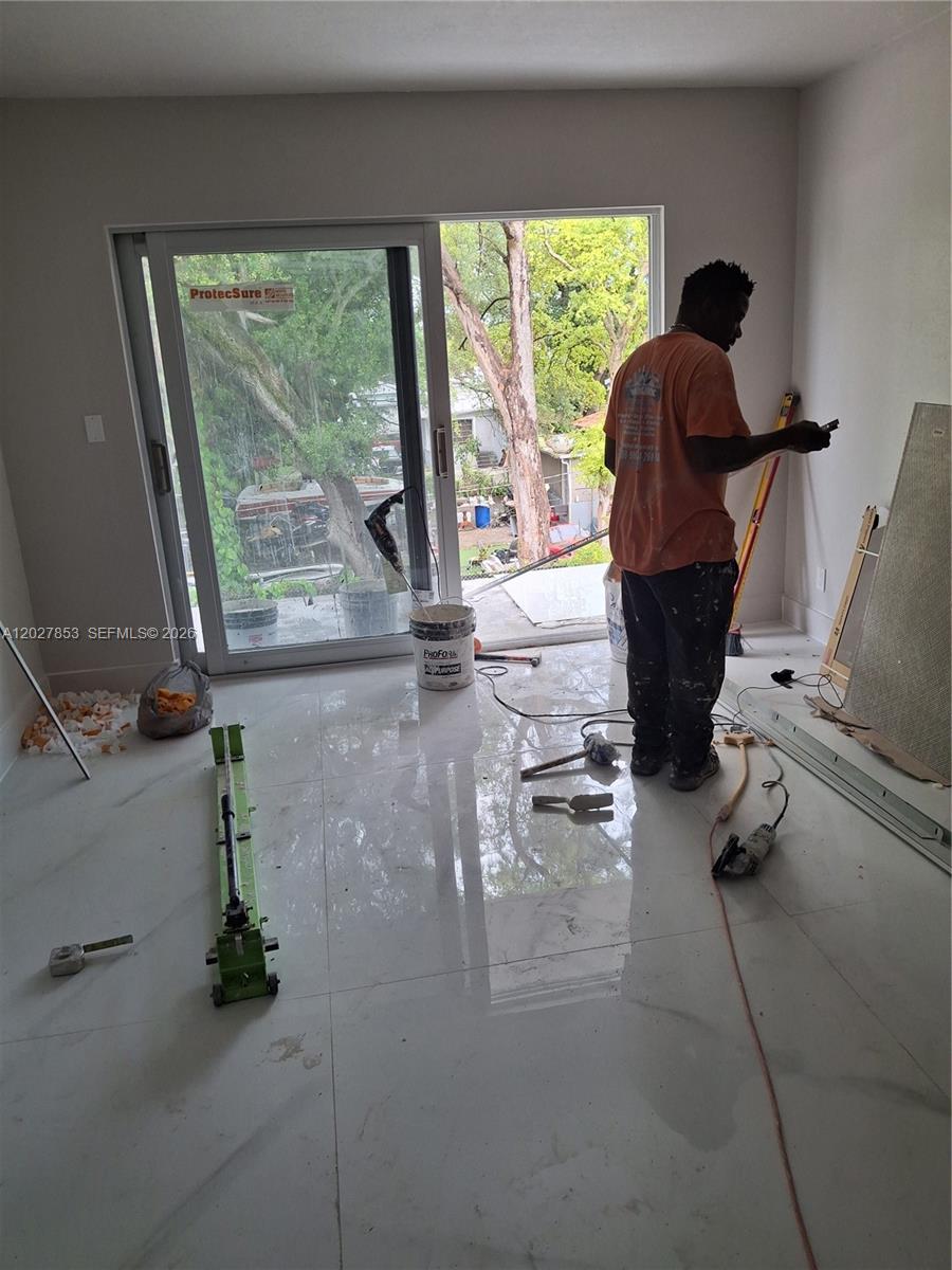 A worker stands in a room with white marble-look tile flooring and a sliding glass door — 13480 NE 6th Ave # 207, North Miami FL 33161, NORTH MIAMI, FL