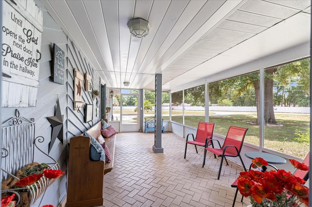 A screened-in porch with a brick-patterned floor, a wooden bench, and red chairs — 11470 SE 73RD COURT, BELLEVIEW, FL