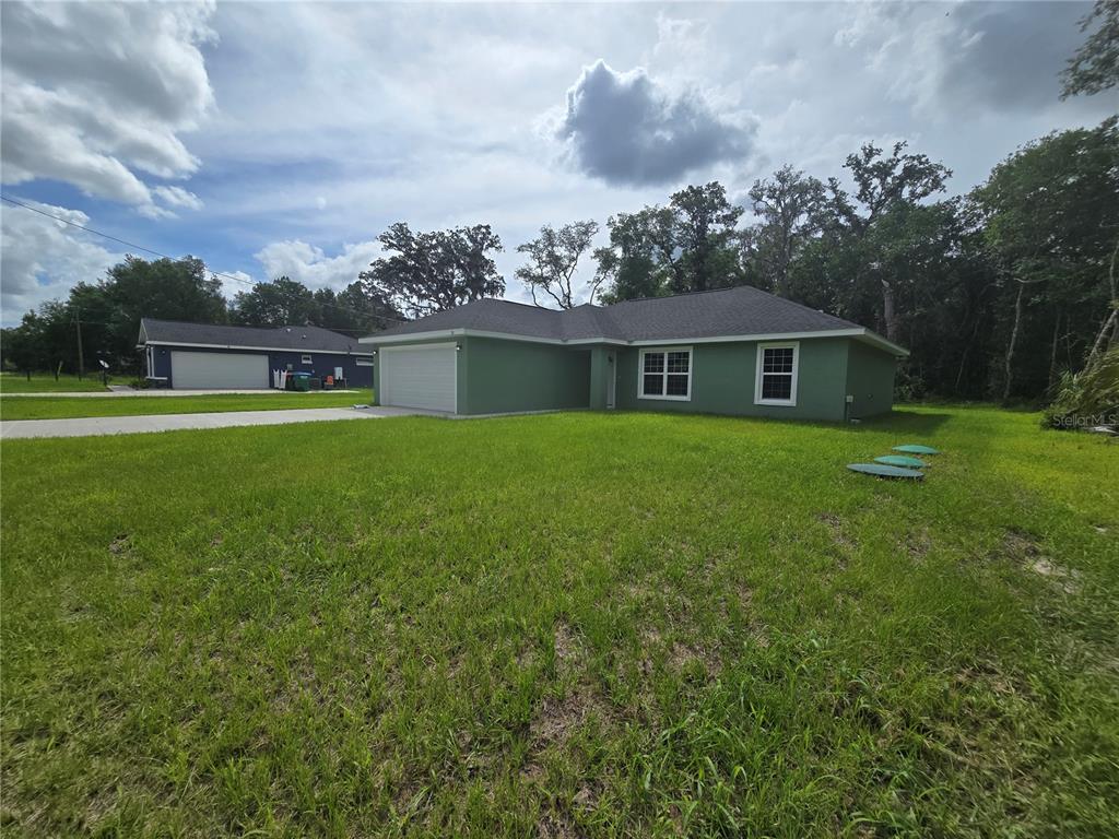 A green single-story house with a two-car garage sits on a large grassy lot — 30 SEQUOIA DRIVE TRACE, OCKLAWAHA, FL