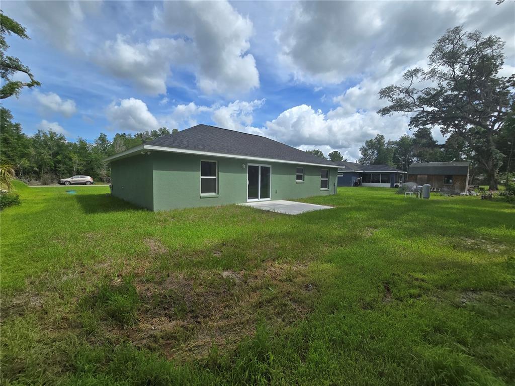 The rear exterior of a green single-story house features a concrete patio and sliding doors — 30 SEQUOIA DRIVE TRACE, OCKLAWAHA, FL