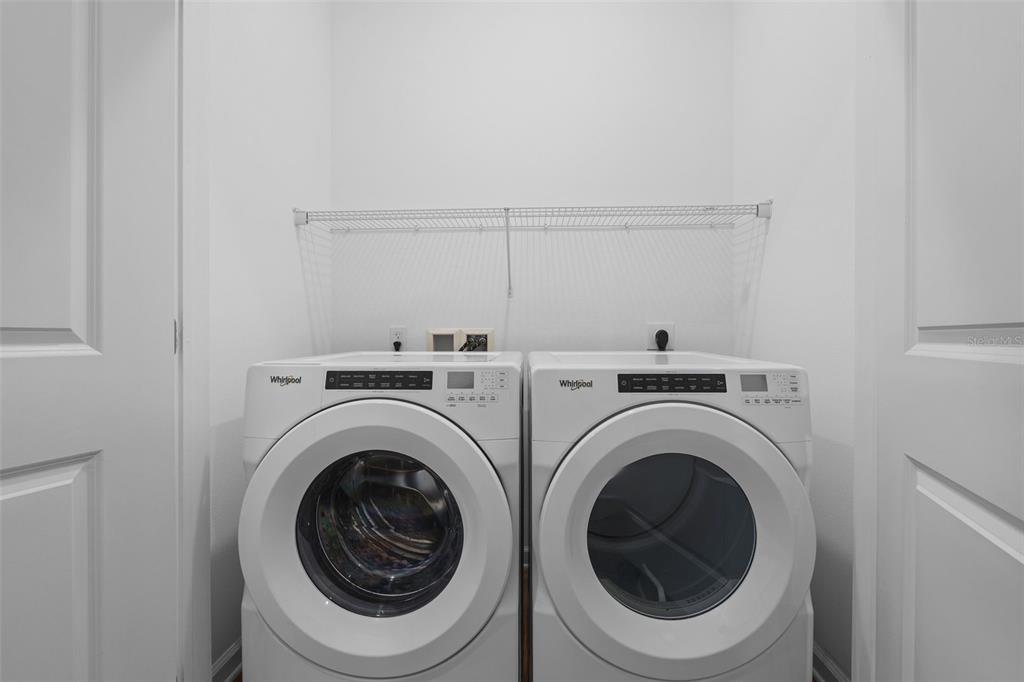 A laundry closet features a side-by-side Whirlpool washer and dryer beneath a wire shelf — 1700 RANCH ROAD UNIT C1A-2201, NOKOMIS, FL