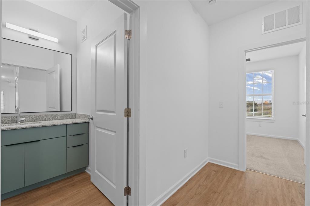 A bathroom vanity with a green cabinet and granite countertop sits beside a carpeted bedroom — 1700 RANCH ROAD UNIT C1A-2201, NOKOMIS, FL