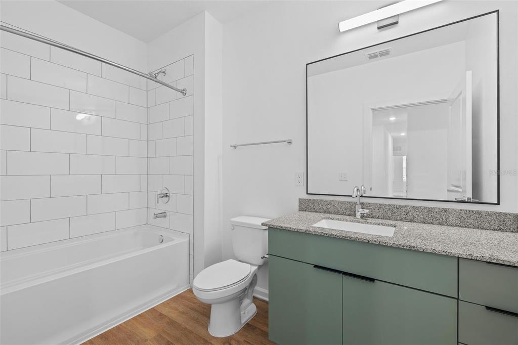 A bathroom features a green vanity, granite countertop, white subway tile shower, and wood flooring — 1700 RANCH ROAD UNIT C1A-2201, NOKOMIS, FL
