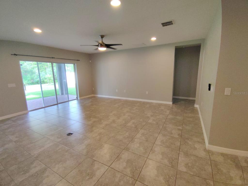 An empty living room features tile flooring, a ceiling fan, and sliding glass patio doors — 2213 WAUKEGAN DRIVE, KISSIMMEE, FL