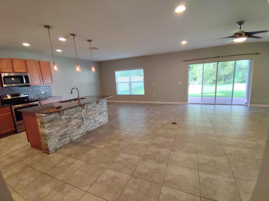 An open-concept kitchen with a stone-faced island and tile flooring leads to a sliding glass door — 2213 WAUKEGAN DRIVE, KISSIMMEE, FL