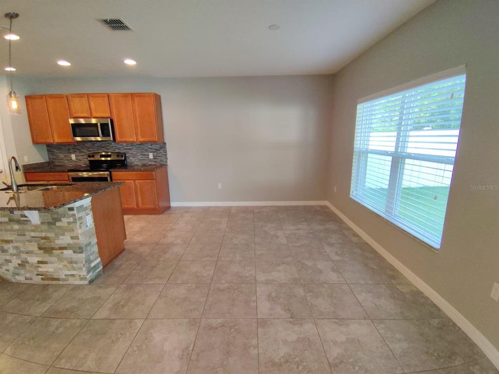 A kitchen with wood cabinets and granite countertops opens to a tiled dining area — 2213 WAUKEGAN DRIVE, KISSIMMEE, FL