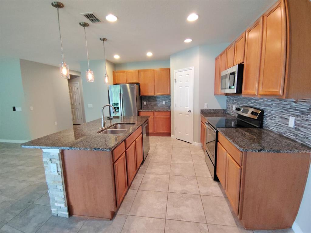 A kitchen with wood cabinets, granite countertops, a center island, and stainless steel appliances — 2213 WAUKEGAN DRIVE, KISSIMMEE, FL