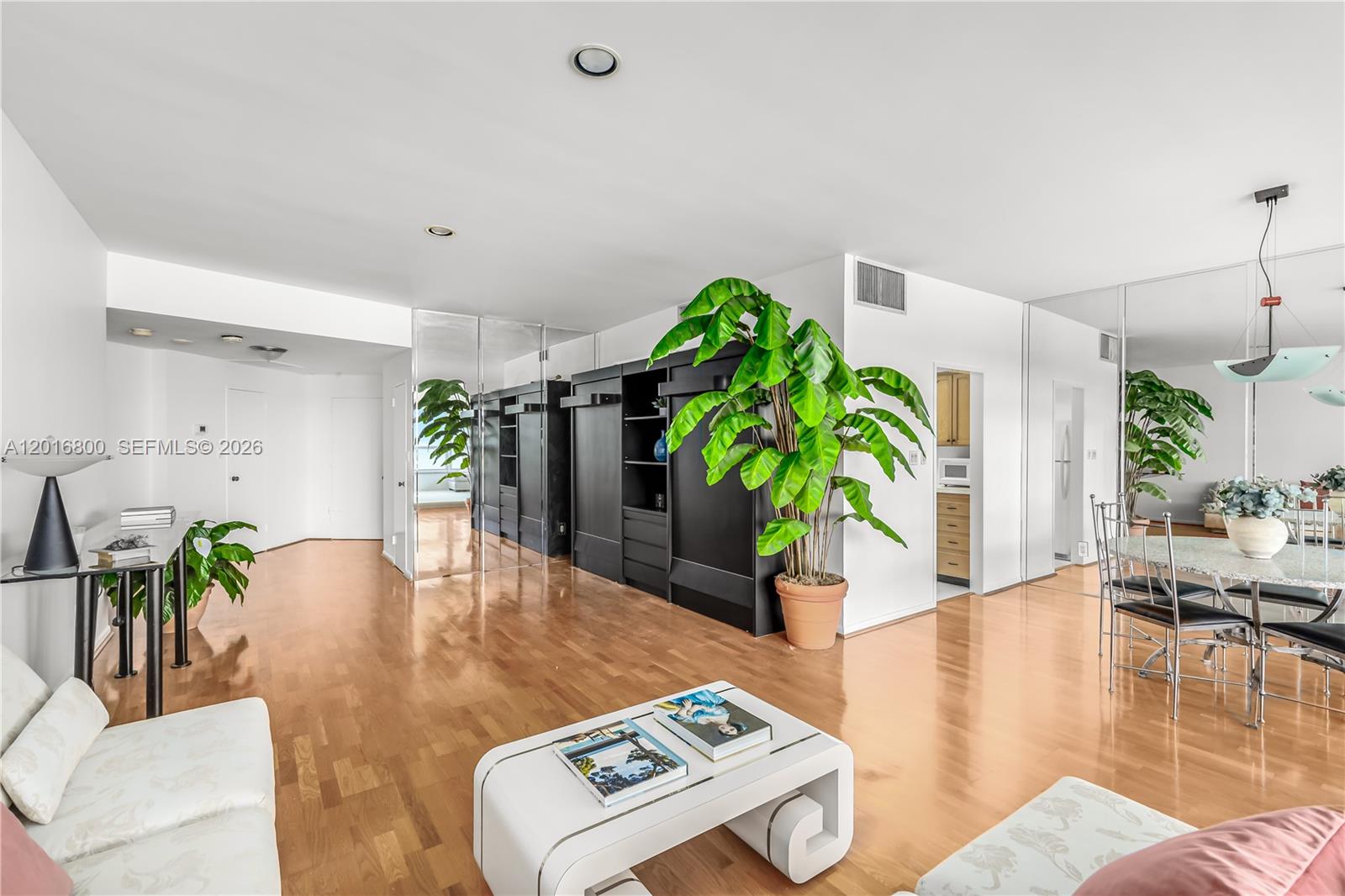 A living and dining area features hardwood floors, mirrored walls, and a large potted plant — 4925 Collins Ave # 5F, Miami Beach FL 33140, MIAMI BEACH, FL