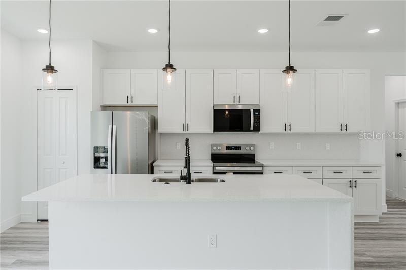 A modern kitchen features white cabinetry, stainless steel appliances, and a large central island — 16204 SW 27TH TERRACE ROAD, OCALA, FL